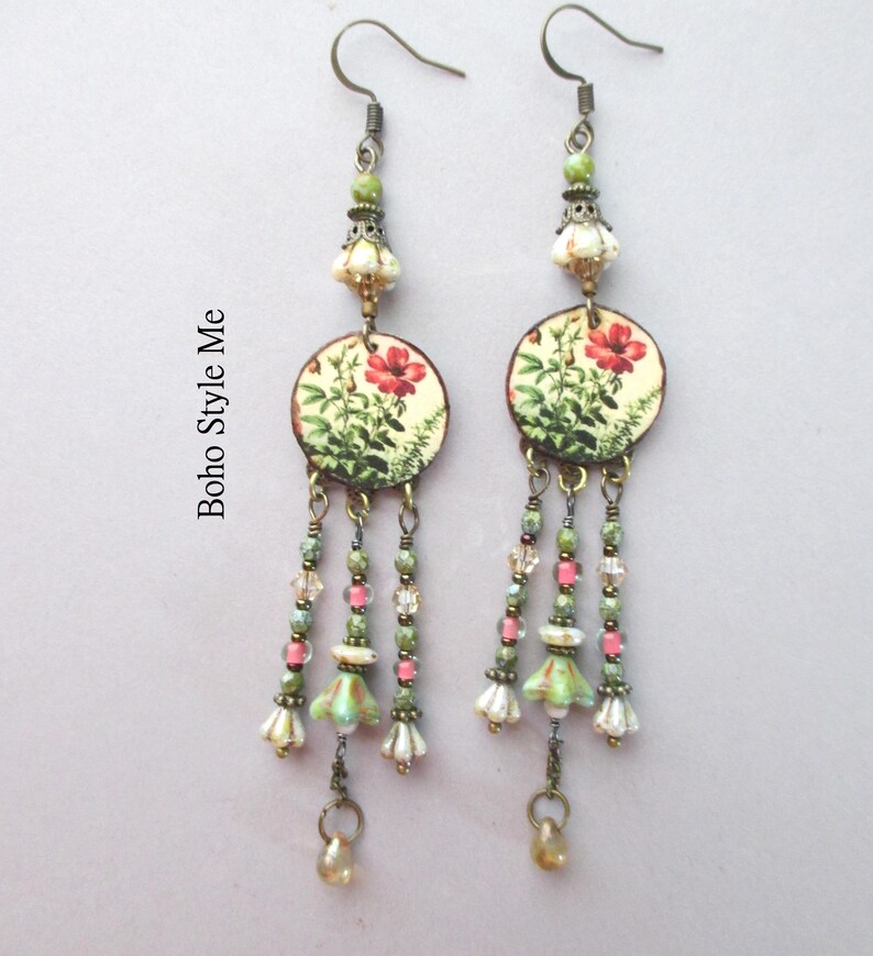 May include: A pair of dangle earrings featuring bronze-toned hooks, green and cream floral-patterned circular discs, and multi-strand drops with green, pink, and clear beads, small bell-shaped charms, and teardrop accents. The text Boho Style Me is visible.