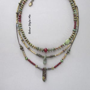 Puede incluir: Un collar de varias hebras con tres capas de cuentas en tonos verde, rojo y oro met&aacute;lico. El dise&ntilde;o incluye peque&ntilde;as cuentas en forma de disco, cuentas rojas redondas y dos colgantes de piedra. El texto Boho Style Me es visible.