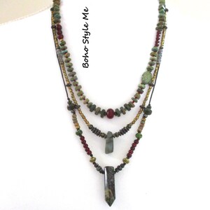 Puede incluir: Un collar de varias hebras con cuentas verdes, marrones y rojas y tres colgantes distintos. El texto "Boho Style Me" est&aacute; impreso verticalmente en el lateral. El dise&ntilde;o incorpora varias cuentas tipo piedra y acentos met&aacute;licos en capas.