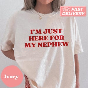 May include: A white t-shirt with the text "I'm just here for my nephew" printed in red.