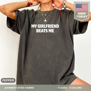 May include: A dark gray t-shirt with the text "MY GIRLFRIEND BEATS ME" printed in white.