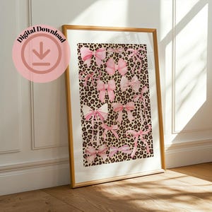 Könnte beinhalten: Gerahmter Druck mit Leopardenmuster-Hintergrund und rosa Schleifen in verschiedenen Größen und Stilen. Der Druck befindet sich in einem goldenen Rahmen und lehnt an einer weißen Wand und einem Holzboden. Der Text "Digital Download" befindet sich in einem rosa Kreis.