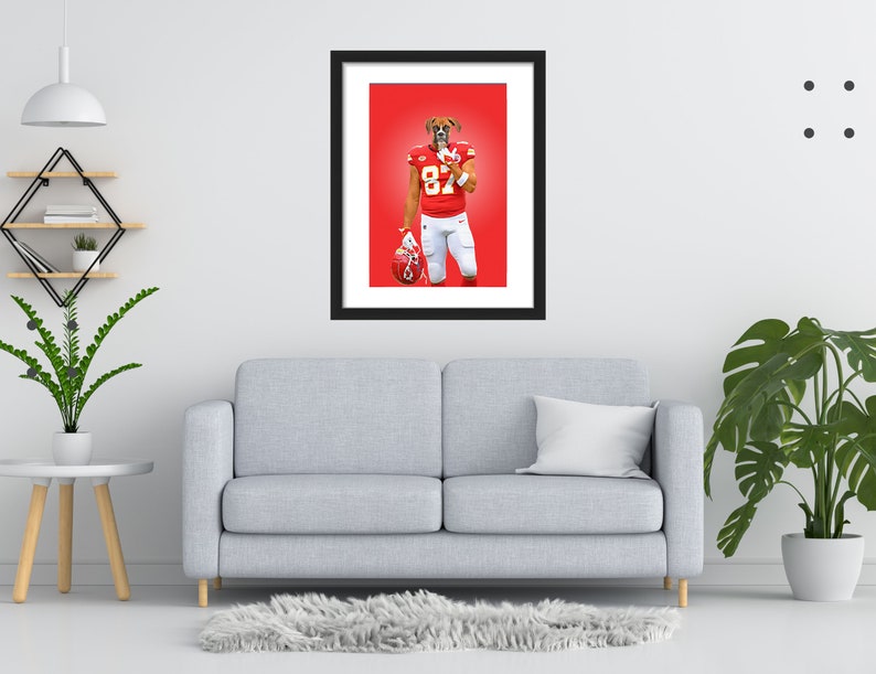 May include: Framed art print showing a boxer dog in a football uniform, number 87. The dog is wearing a red jersey and white trousers, holding a helmet. The background is a solid red. The print is in a black frame.