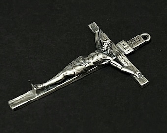May include: A silver-toned crucifix with a detailed depiction of Jesus Christ. The cross features the letters "I.N.R.I." and a loop for hanging. The figure is sculpted with attention to detail, showcasing the religious theme.