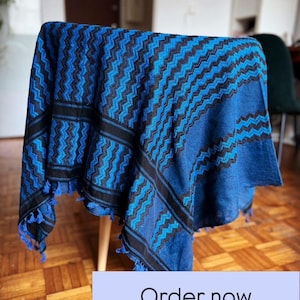 Könnte beinhalten: Blau-schwarzes Textil mit Zickzackmuster, über einem kleinen Tisch drapiert. Das Textil hat eine Fransenborte aus blauen Quasten. Der Text "Order now Limited stock" ist in einem weißen Feld zu sehen.