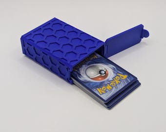 May include: A blue, hexagonal-patterned card storage box with an open lid. The box contains a stack of Pokémon trading cards. The box is made of a solid, durable material and is designed to protect the cards.