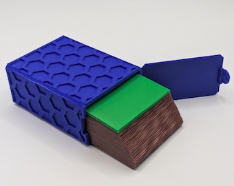 May include: A blue box with a honeycomb pattern on the lid, open to reveal a stack of green and brown cards. The lid is open, revealing the contents. The box is on a white surface.