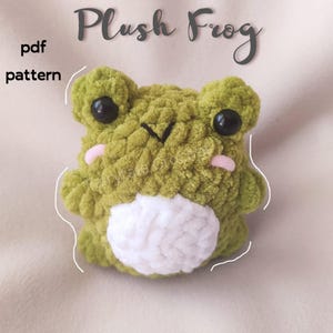 May include: A green crocheted plush frog with white yarn for the belly. The frog has black eyes and pink cheeks. The image includes the text "Plush Frog" and "pdf pattern".
