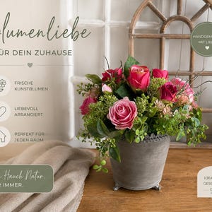 May include: A floral arrangement featuring pink and red roses, green foliage, and sprigs in a gray metal pot. The image includes text that reads "Blumenliebe" and "Ein Hauch Natur."