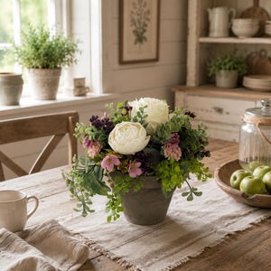 May include: A floral arrangement in a dark grey tapered pot featuring large white peony-like flowers, small pink blossoms, dark purple berries, and various green foliage. The arrangement is displayed as a centrepiece on a wooden table.