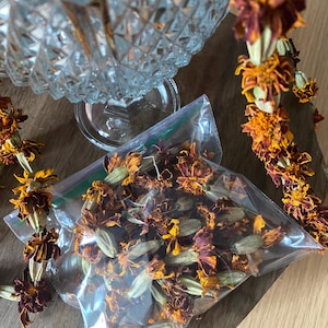 May include: A clear plastic resealable bag filled with dried orange and deep red marigold flowers, accompanied by a string of dried marigold blossoms and a clear glass bowl with a diamond-cut pattern on the exterior surface.