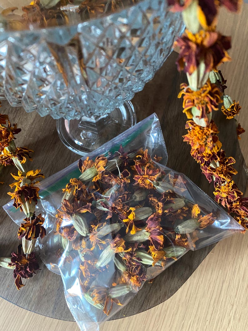 May include: A clear plastic resealable bag filled with dried orange and deep red marigold flowers, accompanied by a string of dried marigold blossoms and a clear glass bowl with a diamond-cut pattern on the exterior surface.
