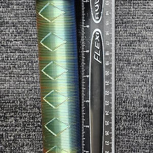 May include: A blue and green bicycle handlebar grip with a diamond pattern. The grip is about 6 inches long and is measured against a ruler.