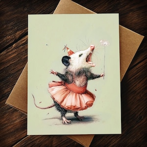 K&ouml;nnte beinhalten: Eine skurrile Gru&szlig;karte mit einem Opossum in einem rosa Tutu und einer Partyh&uuml;tchen, das einen Wunderkerzenstab h&auml;lt. Das Opossum hat den Mund offen. Die Karte befindet sich auf einem hellgr&uuml;nen Hintergrund mit einem braunen Umschlag.
