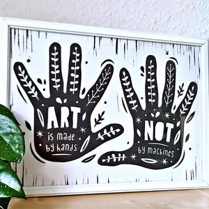 May include: A framed art print with a white border. The black and white artwork features two stylized handprints with botanical details. The text reads "ART is made by hands, NOT by machines."