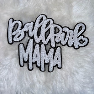 Puede incluir: Un letrero decorativo en blanco y negro con las palabras "Ballpark MAMA" en fuente cursiva. Las letras blancas tienen una textura punteada, delineadas en negro, sobre un fondo blanco y esponjoso.