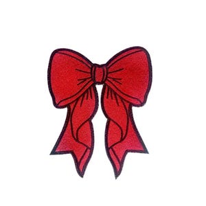 Puede incluir: Un lazo de tela rojo con contornos negros. El lazo está atado en un nudo y tiene dos colas largas.