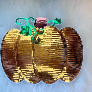Peut inclure: Une citrouille dorée en sequins avec une tige et des feuilles vertes. La citrouille est un patch décoratif pour les vêtements ou l'artisanat.