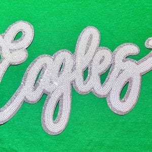 May include: White sequined patch with the word "Eagles" in a cursive font.