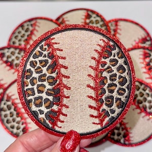 Puede incluir: Un conjunto de parches con temática de béisbol. Cada parche presenta un diseño de béisbol con costuras rojas y un acento de estampado de leopardo. Los bordes están adornados con purpurina roja. Los parches son redondos y parecen bordados.