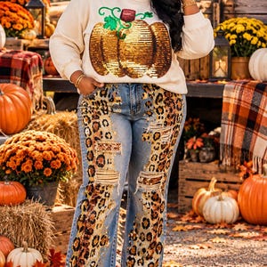 Puede incluir: Una sudadera de manga larga color crema con un gráfico de calabaza de lentejuelas en la parte delantera, combinada con unos vaqueros de mezclilla azul claro con secciones desgastadas y paneles de lentejuelas con estampado de leopardo.