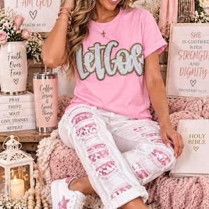 May include: A light pink t-shirt with the text "let Go" in silver and gold sequins, paired with white distressed jeans featuring pink sequin patches on the thighs and white sneakers with pink star accents on the sides.