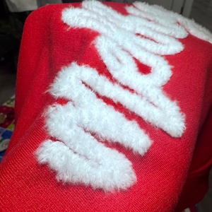 Peut inclure: Gros plan sur un textile rouge avec des lettres blanches et duveteuses. Les lettres blanches semblent épeler un mot ou une phrase. Le tissu a un aspect texturé.