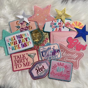 May include: A collection of colorful iron-on patches with various sayings and designs, including "Boat Waves Sun Rays Lake Days", "Talk Dirty To Me", "You Had Me At Day Drinking", "Howdy Cowboy", "Coors Cowboy", "I Like Hot Mommas", "Babewe", "Put On My Husbands Tab", and "The Original".