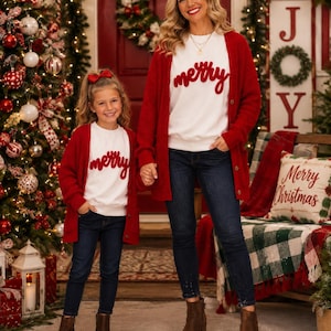 May include: Two matching outfits consisting of a white sweatshirt with the red cursive text merry, a long-sleeved red button-down cardigan, dark blue denim jeans, and brown ankle boots. The smaller outfit includes a red hair bow accessory.