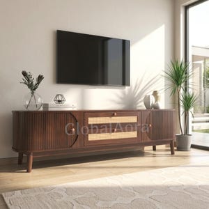 May include: A dark wood media console featuring two side cabinets with vertical fluted detailing and a central section with two drawers accented by woven cane panels and small round knobs, supported by four tapered legs on a light wood floor.