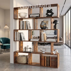 May include: A tall, open-concept bookshelf with a dark wood grain finish, featuring multiple rectangular storage compartments. The shelves are filled with various books, a woven basket, decorative glass bowls, a black sculpture, and a lamp.