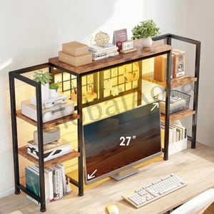 May include: A wooden and metal TV stand with a 27-inch monitor. The stand has multiple shelves for storage, with books, speakers, and decorative items. The stand has a black metal frame and brown wooden shelves.