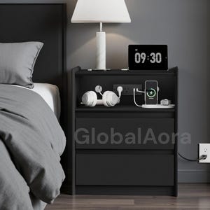 May include: Black nightstand with two drawers, a shelf, and built-in charging ports. A white lamp with a cylindrical base sits on top, along with a tablet displaying 09:30. White headphones and a charging phone are visible.