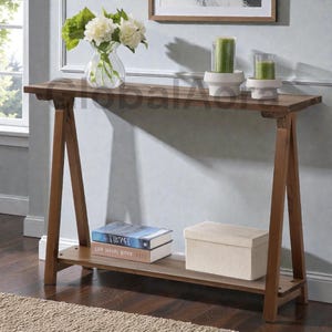 May include: A wooden console table with a dark brown finish. The table has a rectangular top and a lower shelf. A glass vase with white flowers, two green candles, two books, and a beige box are on the table.