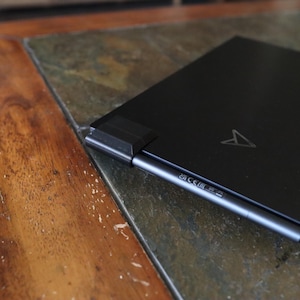 May include: A black laptop computer with a silver stylus attached to the side. The laptop has a logo on the lid and the text "EA CE EU" on the side.