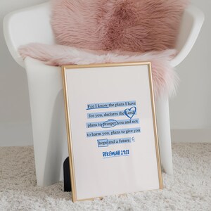 Puede incluir: Una impresi&oacute;n enmarcada con borde dorado muestra el texto "For I know the plans I have for you..." en azul. La impresi&oacute;n descansa contra una silla blanca con una manta de piel sint&eacute;tica rosa, sobre una alfombra blanca.