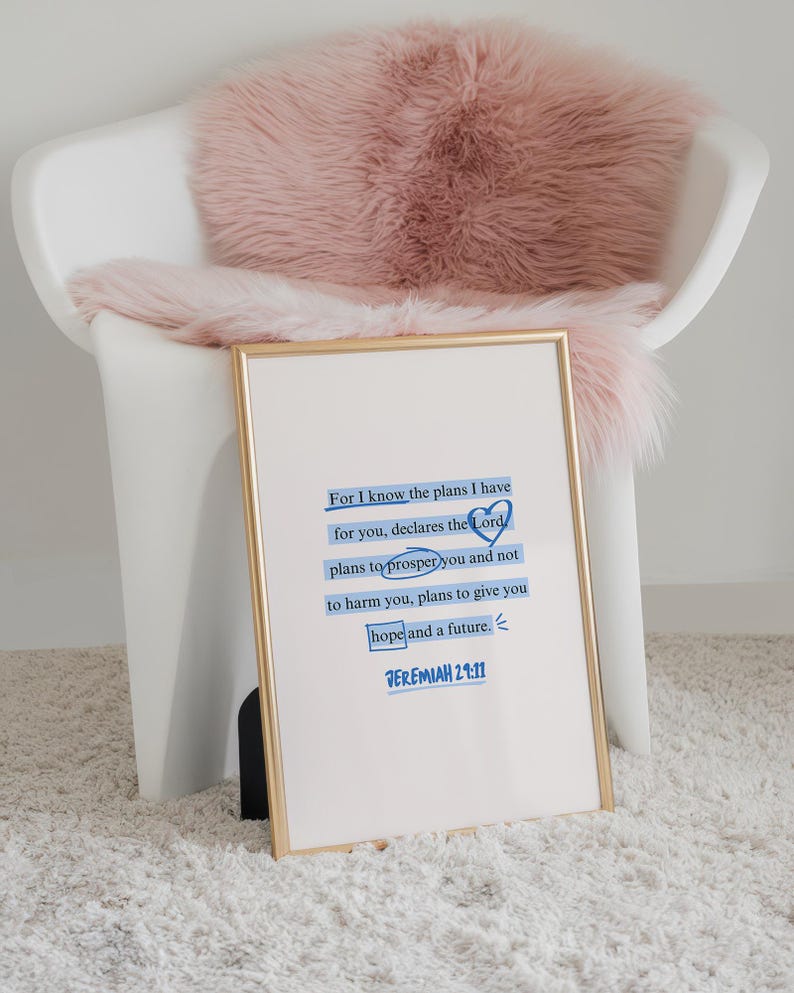 Puede incluir: Una impresi&oacute;n enmarcada con borde dorado muestra el texto "For I know the plans I have for you..." en azul. La impresi&oacute;n descansa contra una silla blanca con una manta de piel sint&eacute;tica rosa, sobre una alfombra blanca.