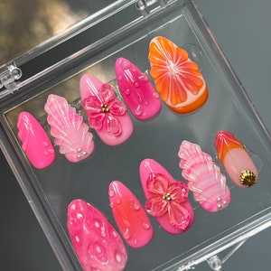 Puede incluir: Un conjunto de diez uñas postizas de color rosa y naranja con varios diseños, incluyendo flores, hojas y una rodaja de cítricos.