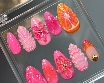 May include: A set of ten pink and orange press-on nails with various designs, including flowers, leaves, and a citrus fruit slice.