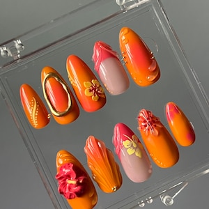 May include: A set of ten orange and pink artificial nails with floral designs. The nails are in a clear plastic case.