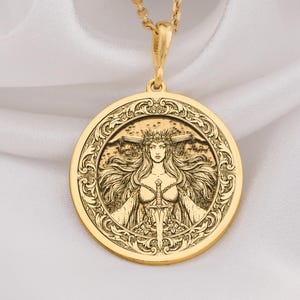 Può includere: Una collana con pendente dorato con un design inciso dettagliato di una donna con capelli fluenti e una corona, incorniciato in un cerchio. Il pendente è appeso a una delicata catena, creando un accessorio elegante.