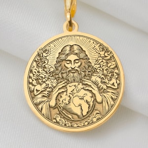 May include: A gold-colored pendant necklace featuring a circular medallion with a detailed relief of a religious figure holding the Earth. The pendant is suspended from a delicate gold chain, set against a white fabric background.