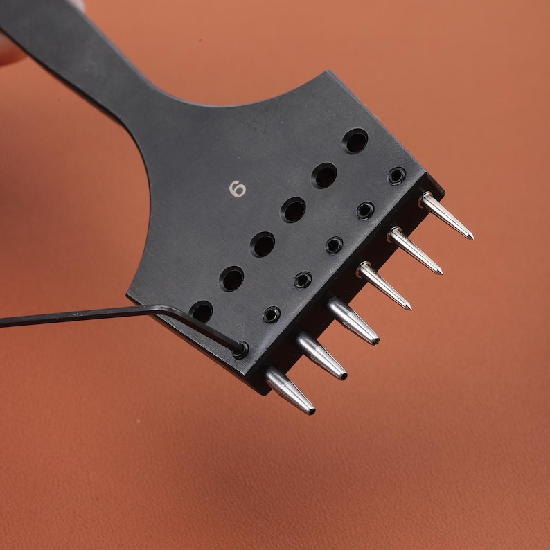May include: Black leather punch tool with six needles and a numbered dial that reads "6".