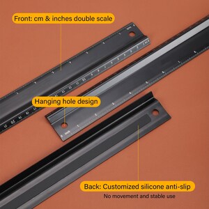 May include: Black metal ruler with a double scale in centimeters and inches. The ruler has a hanging hole design and a black silicone anti-slip back. The text on the ruler reads "Front: cm & inches double scale" and "Hanging hole design". The text on the back of the ruler reads "Back: Customized silicone anti-slip No movement and stable use".