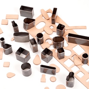 May include: A set of leather craft tools, including various shapes and sizes of metal punches, a leather cutting mat, and leather scraps. The punches are used to create holes and shapes in leather for crafting projects.