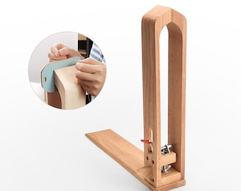 Puede incluir: Un caballete de madera para coser cuero con una abrazadera y una palanca roja. El caballete se utiliza para sujetar el cuero mientras se cose.