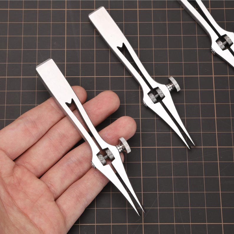 May include: Two silver metal calipers with adjustable points. The calipers are used for measuring the width of objects.