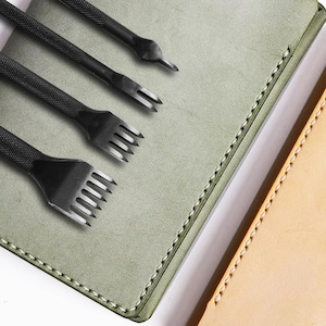 May include: A set of four leather stitching tools with different sized prongs. The tools are laid out on a green leather surface with a brown leather surface in the background.