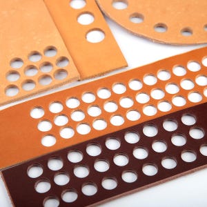 May include: Four pieces of leather with different sized holes punched in them. The leather is in shades of brown and dark brown.
