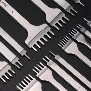 May include: A set of six silver leather stitching tools with different sized needles. The tools are arranged in a staggered pattern on a black background. The tools are labeled with the numbers 4, 4, 6, and 6.